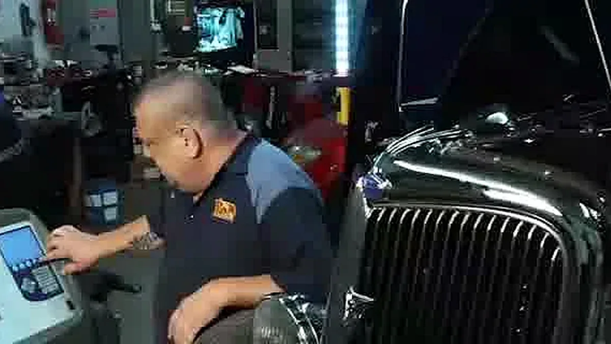 Technician using diagnostic equipment beside a vehicle in the repair shop